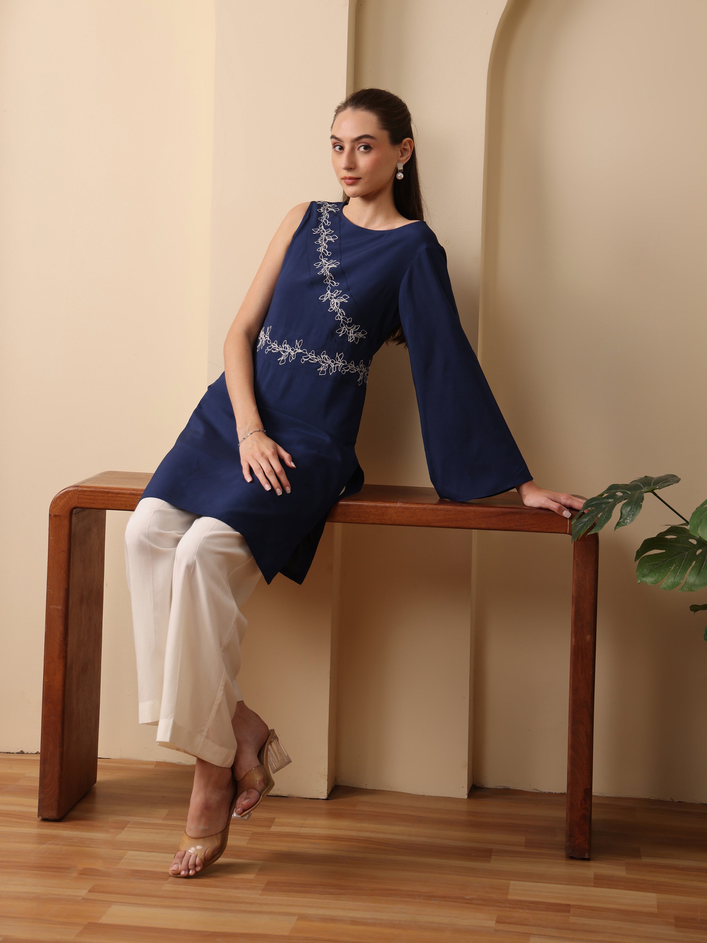 Woman in navy blue one-shoulder tunic with silver embroidery and cream wide-leg trousers